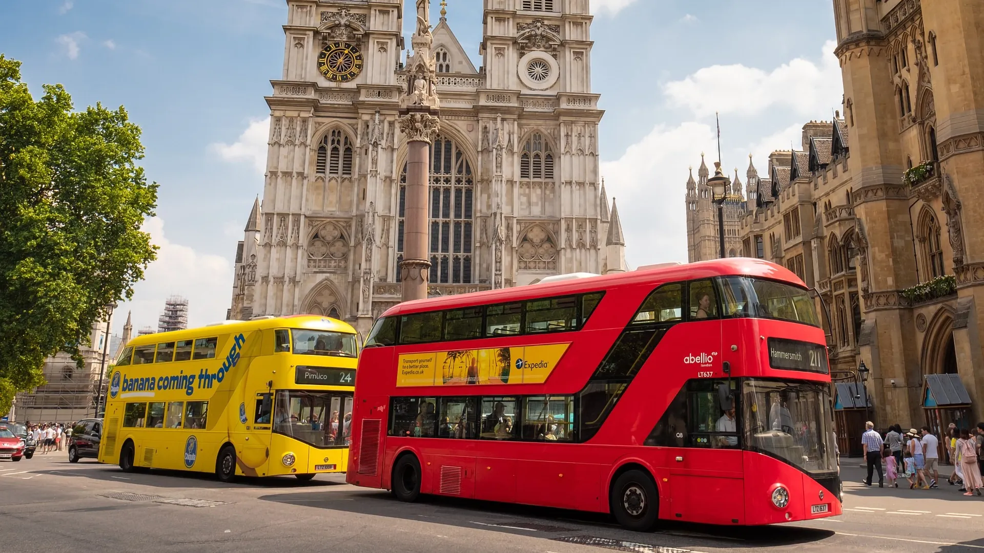 Two branded London red buses passing by the Palace of Westminster in London