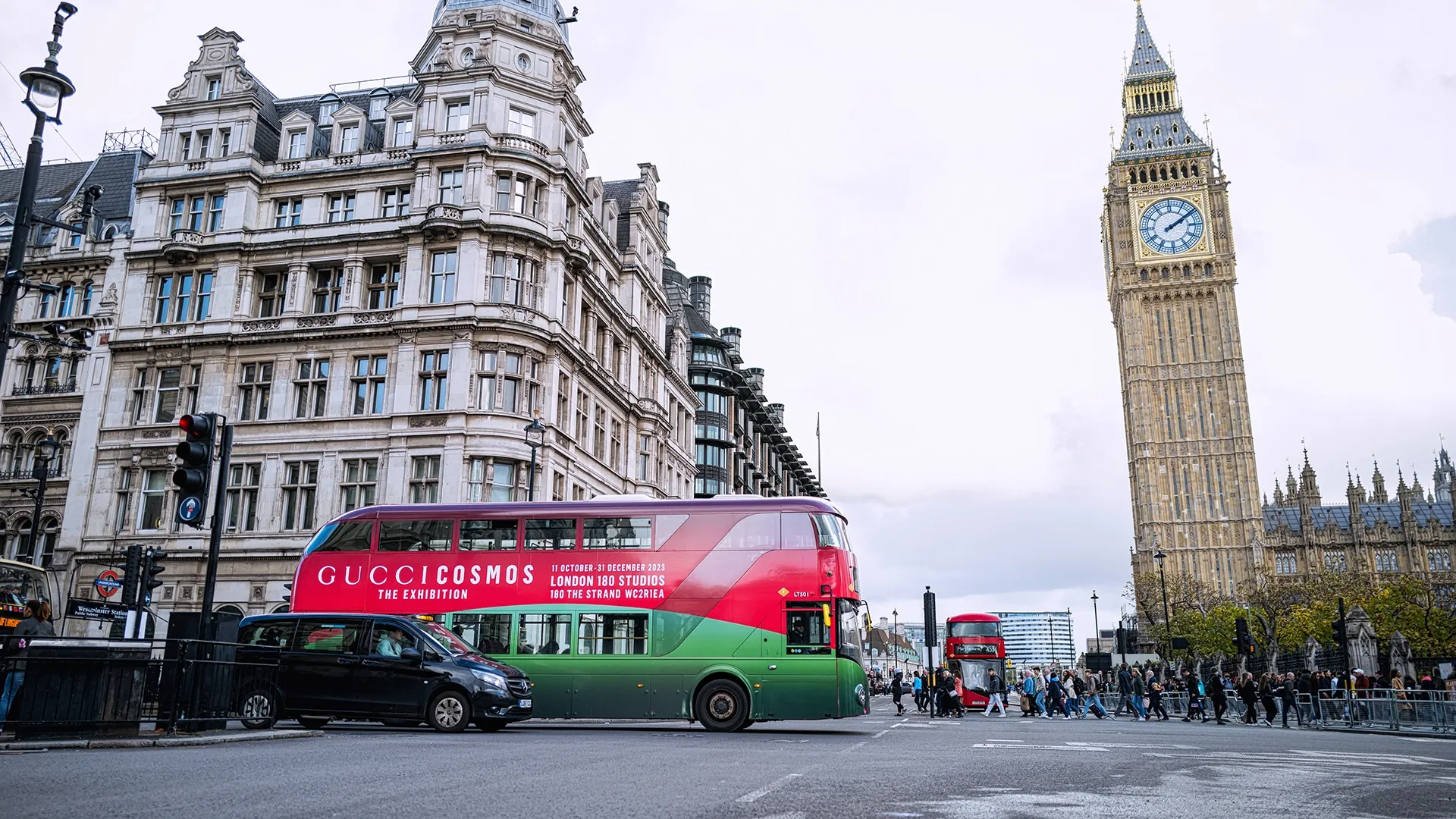 A Gucci-wrapped red London bus travelling past Big Ben in Westminster, London