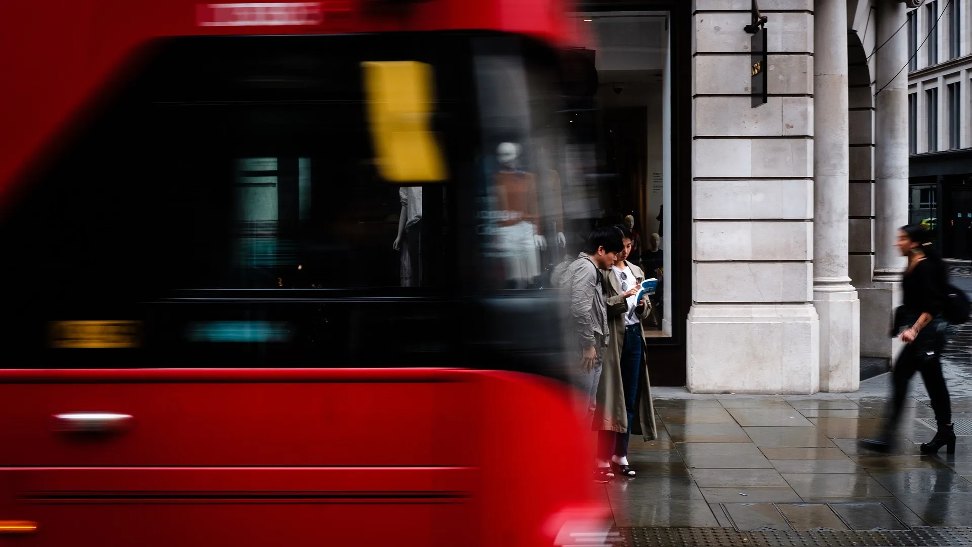 Two people look at a book on a busy London street as a bus passes by in the foreground